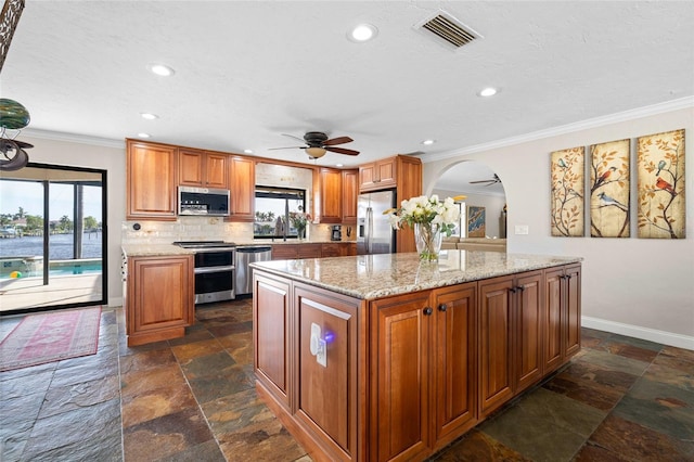 kitchen with ceiling fan, a center island, tasteful backsplash, light stone counters, and appliances with stainless steel finishes