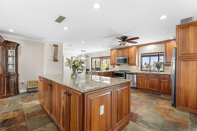 kitchen with appliances with stainless steel finishes, backsplash, light stone counters, ceiling fan, and a kitchen island