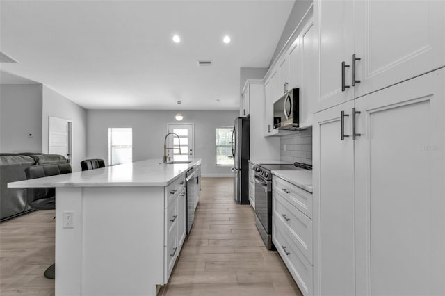 kitchen with a kitchen island with sink, white cabinets, a kitchen breakfast bar, light hardwood / wood-style flooring, and appliances with stainless steel finishes