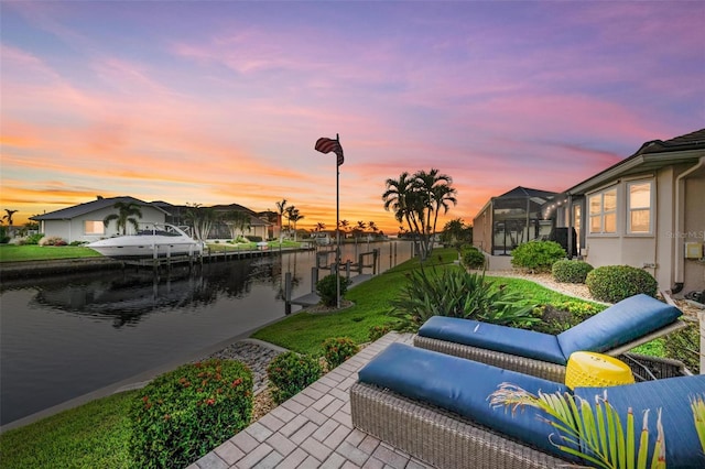 patio terrace at dusk featuring a yard, a water view, and a lanai