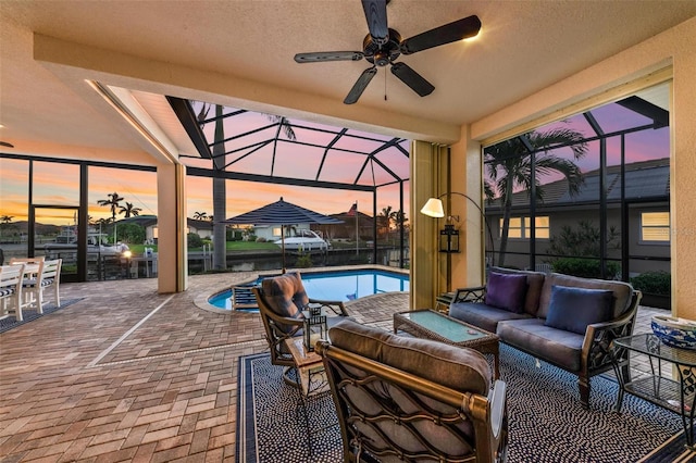 patio terrace at dusk featuring an outdoor living space, ceiling fan, and a lanai