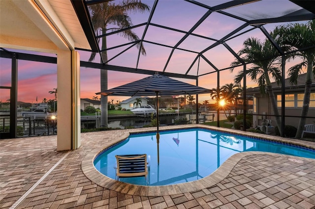 pool at dusk with glass enclosure, a water view, and a patio