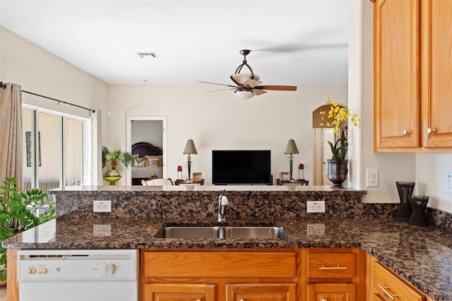 kitchen featuring dishwasher, sink, ceiling fan, dark stone countertops, and kitchen peninsula