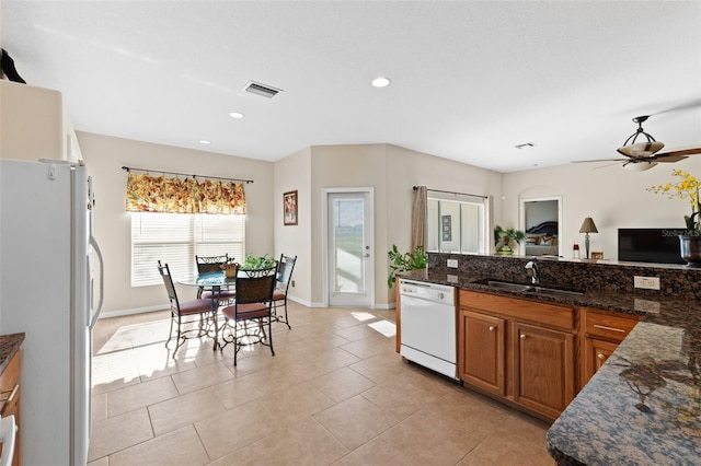 kitchen with dark stone counters, white appliances, ceiling fan, sink, and light tile patterned flooring