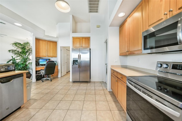 kitchen featuring a towering ceiling, built in desk, light tile patterned floors, and stainless steel appliances