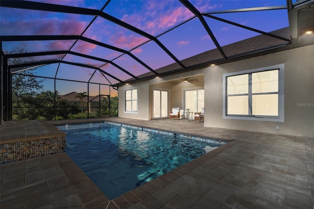 pool at dusk featuring a patio, glass enclosure, and ceiling fan