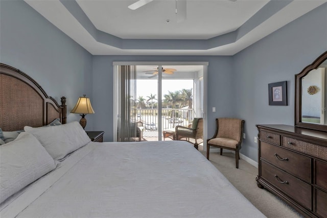 bedroom featuring ceiling fan, access to exterior, light carpet, and a tray ceiling