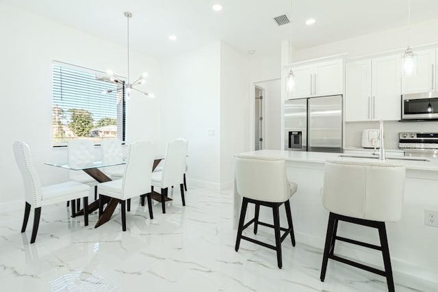 kitchen with an inviting chandelier, appliances with stainless steel finishes, white cabinets, and decorative light fixtures