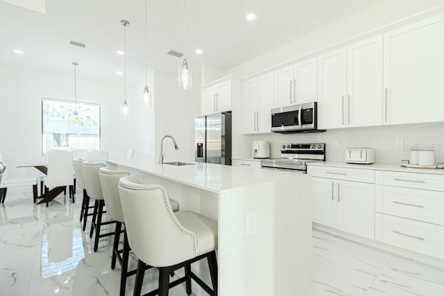 kitchen with stainless steel appliances, a kitchen island with sink, white cabinets, and decorative light fixtures