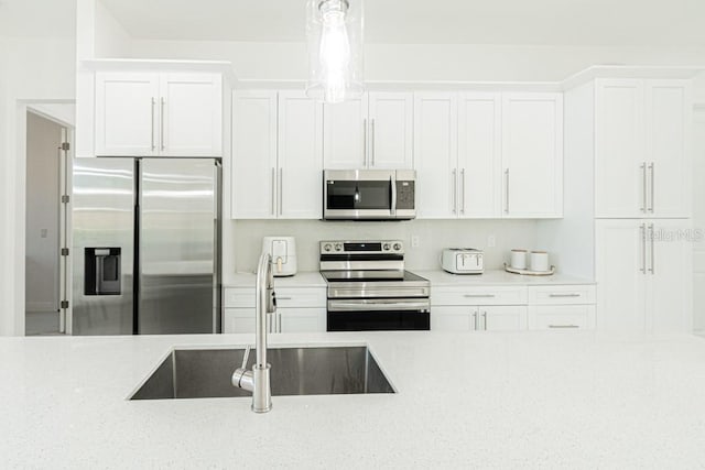 kitchen with white cabinetry, stainless steel appliances, hanging light fixtures, light stone countertops, and sink