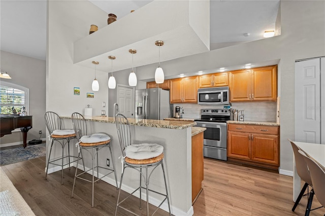 kitchen with a breakfast bar area, appliances with stainless steel finishes, decorative backsplash, and hanging light fixtures