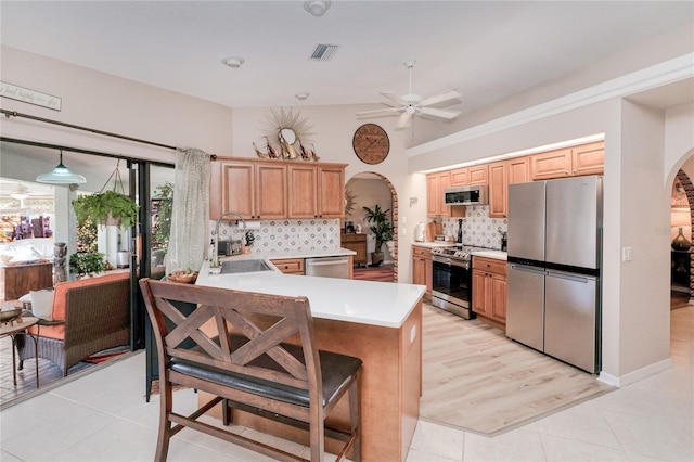 kitchen featuring ceiling fan, light tile patterned floors, tasteful backsplash, kitchen peninsula, and stainless steel appliances