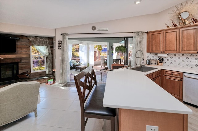 kitchen featuring dishwasher, sink, decorative backsplash, a large fireplace, and kitchen peninsula