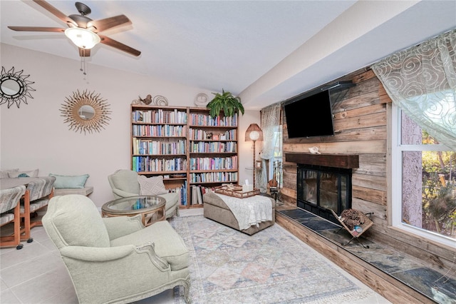 living room with ceiling fan, a large fireplace, light hardwood / wood-style floors, and wood walls