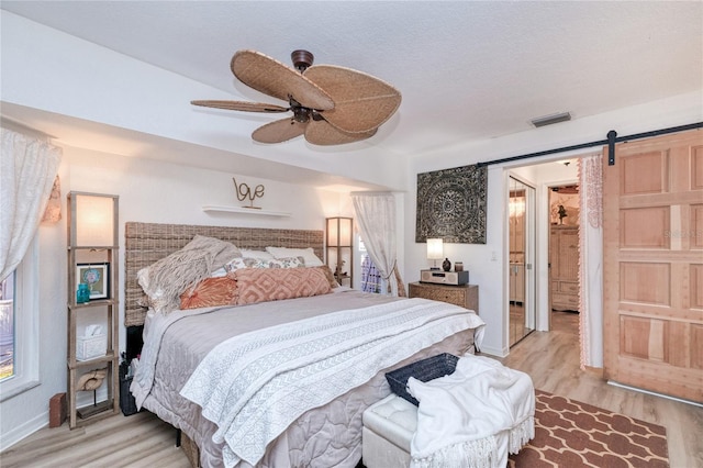 bedroom featuring ceiling fan, a barn door, a textured ceiling, and light hardwood / wood-style flooring