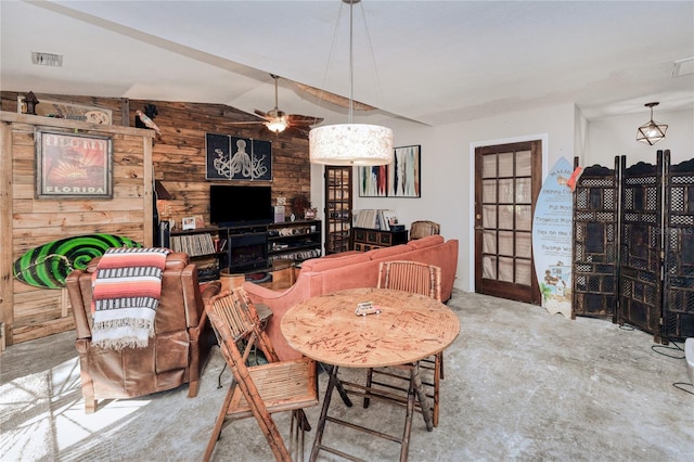 dining space with concrete floors, vaulted ceiling, ceiling fan, and wooden walls