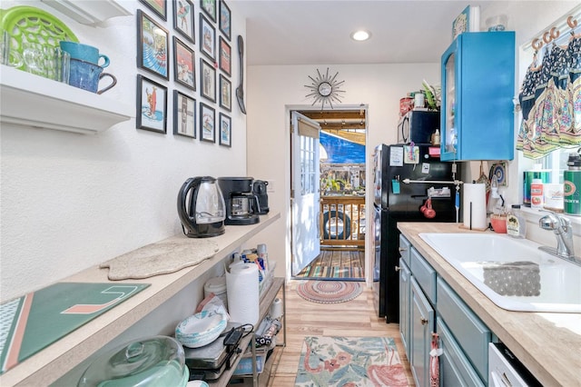 kitchen featuring dishwasher, black fridge, sink, blue cabinetry, and light hardwood / wood-style floors