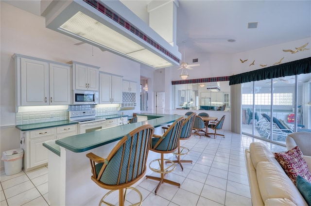 kitchen featuring range with electric cooktop, light tile patterned floors, a kitchen breakfast bar, backsplash, and white cabinets