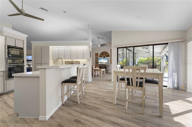 kitchen featuring a kitchen breakfast bar, light wood-type flooring, sink, black appliances, and high vaulted ceiling