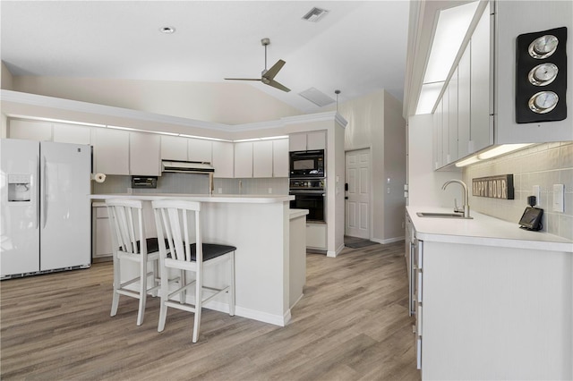 kitchen featuring a breakfast bar, white cabinets, black appliances, and vaulted ceiling