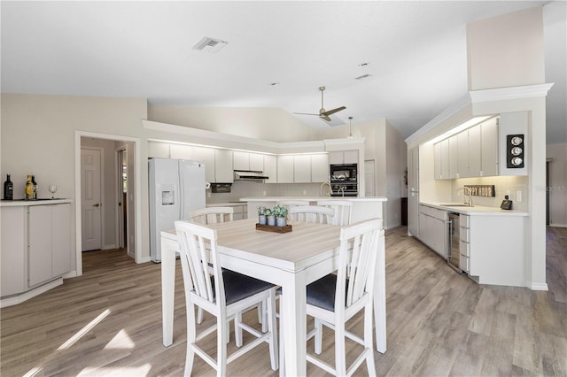 dining area with ceiling fan, sink, vaulted ceiling, and light wood-type flooring