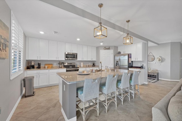 kitchen featuring light stone countertops, stainless steel appliances, a kitchen island with sink, white cabinets, and hanging light fixtures