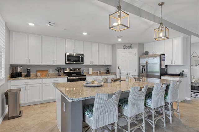 kitchen with white cabinets, pendant lighting, an island with sink, and appliances with stainless steel finishes