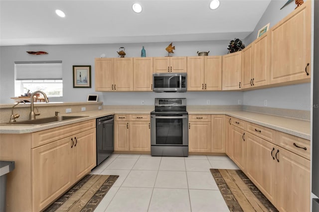 kitchen with light brown cabinetry, stainless steel appliances, vaulted ceiling, sink, and light tile patterned floors