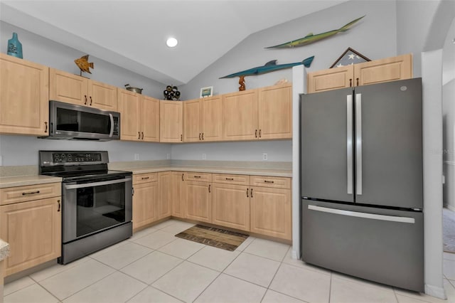 kitchen with light brown cabinetry, stainless steel appliances, lofted ceiling, and light tile patterned flooring