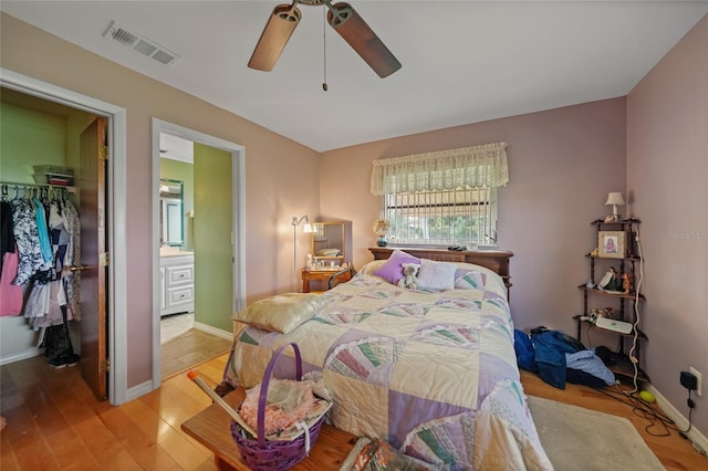 bedroom with a walk in closet, light wood-type flooring, ensuite bath, ceiling fan, and a closet