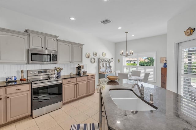 kitchen featuring sink, stainless steel appliances, dark stone counters, a chandelier, and light tile patterned floors