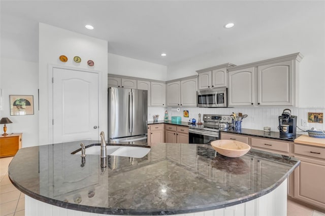 kitchen featuring dark stone counters, stainless steel appliances, sink, light tile patterned floors, and a center island