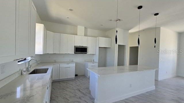 kitchen featuring white cabinetry, a center island, light stone countertops, sink, and pendant lighting