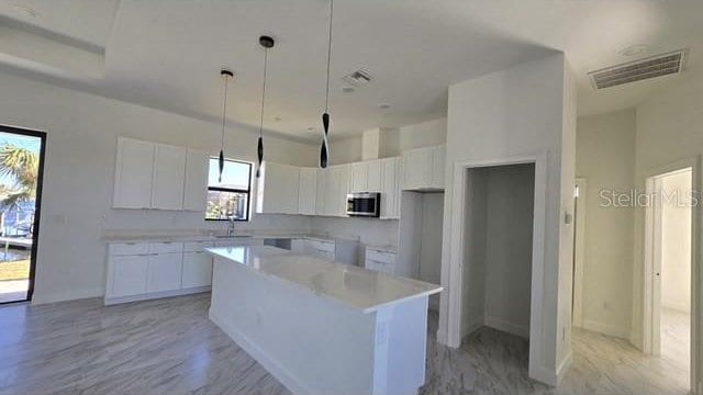 kitchen featuring white cabinets, pendant lighting, a center island, and sink