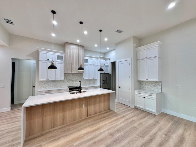 kitchen with a kitchen island with sink, hanging light fixtures, stainless steel fridge, white cabinets, and sink