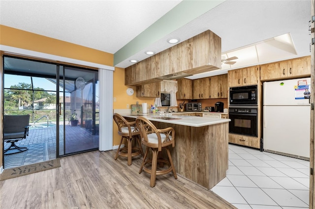 kitchen with ceiling fan, kitchen peninsula, light hardwood / wood-style floors, a breakfast bar area, and black appliances