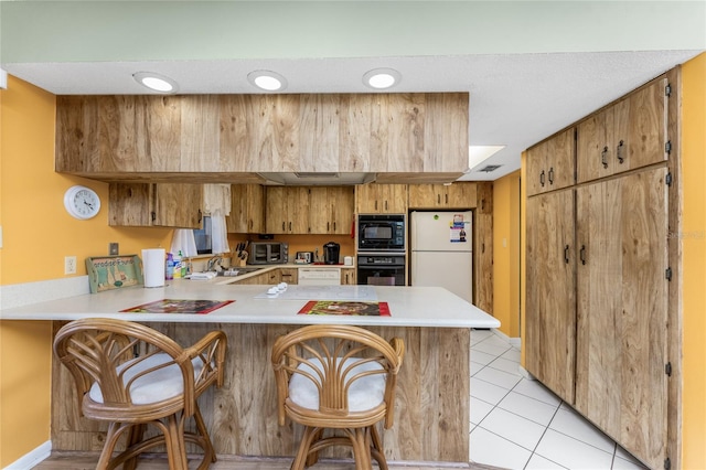 kitchen featuring a breakfast bar, black appliances, sink, light tile patterned floors, and kitchen peninsula