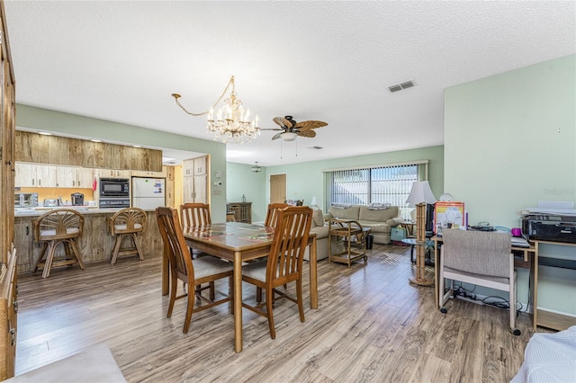 dining room with ceiling fan with notable chandelier, light wood-type flooring, and a textured ceiling