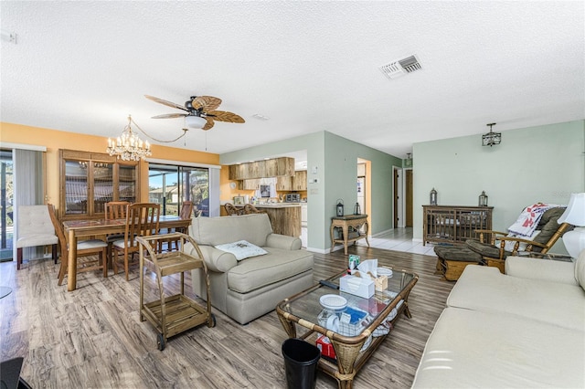 living room with a textured ceiling, ceiling fan with notable chandelier, and light hardwood / wood-style flooring