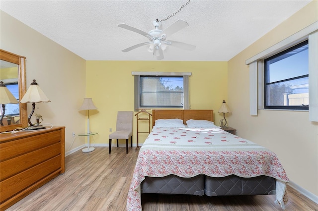 bedroom featuring a textured ceiling, light hardwood / wood-style floors, multiple windows, and ceiling fan