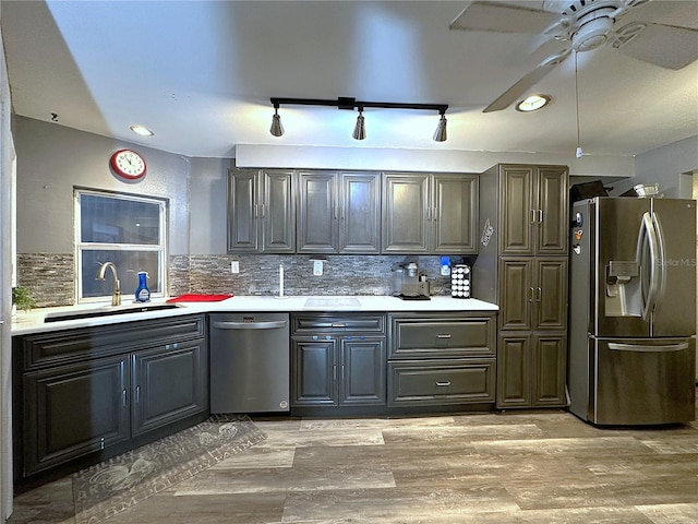 kitchen featuring appliances with stainless steel finishes, backsplash, rail lighting, sink, and light hardwood / wood-style floors