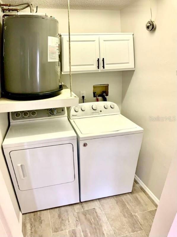 clothes washing area featuring cabinets, water heater, light hardwood / wood-style floors, a textured ceiling, and washer and clothes dryer