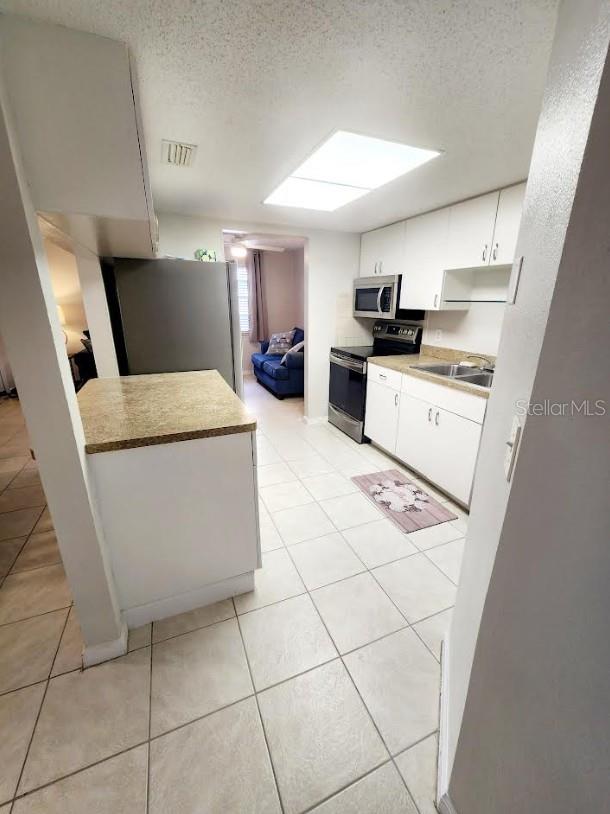 kitchen featuring white cabinets, light tile patterned flooring, a textured ceiling, and appliances with stainless steel finishes