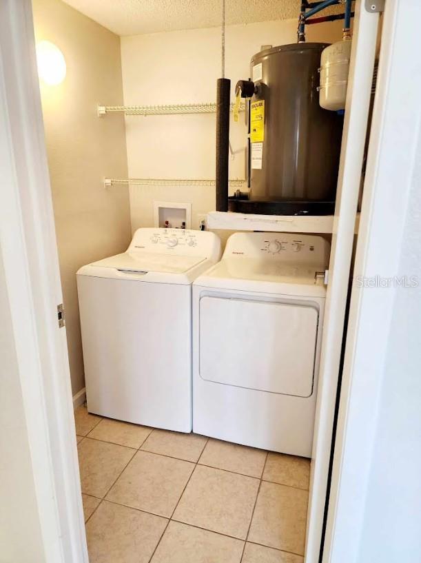 washroom with washing machine and clothes dryer, water heater, and light tile patterned floors