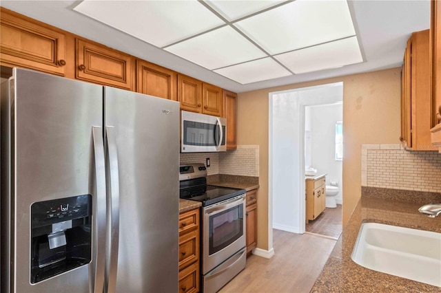 kitchen with backsplash, sink, light hardwood / wood-style flooring, and appliances with stainless steel finishes