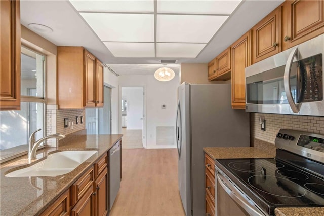 kitchen with backsplash, sink, light hardwood / wood-style flooring, light stone countertops, and stainless steel appliances