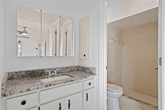 bathroom with vanity, ceiling fan, toilet, and a tile shower