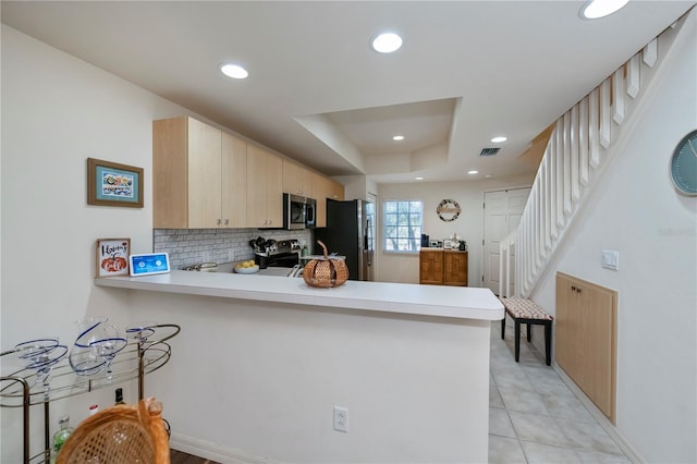 kitchen featuring a raised ceiling, stainless steel appliances, a peninsula, and light countertops