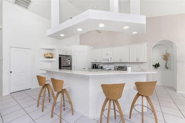 kitchen featuring a kitchen breakfast bar, white appliances, high vaulted ceiling, white cabinets, and light tile patterned flooring