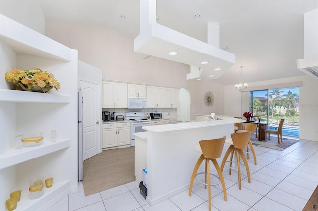 kitchen featuring white appliances, high vaulted ceiling, white cabinetry, a breakfast bar area, and light tile patterned flooring